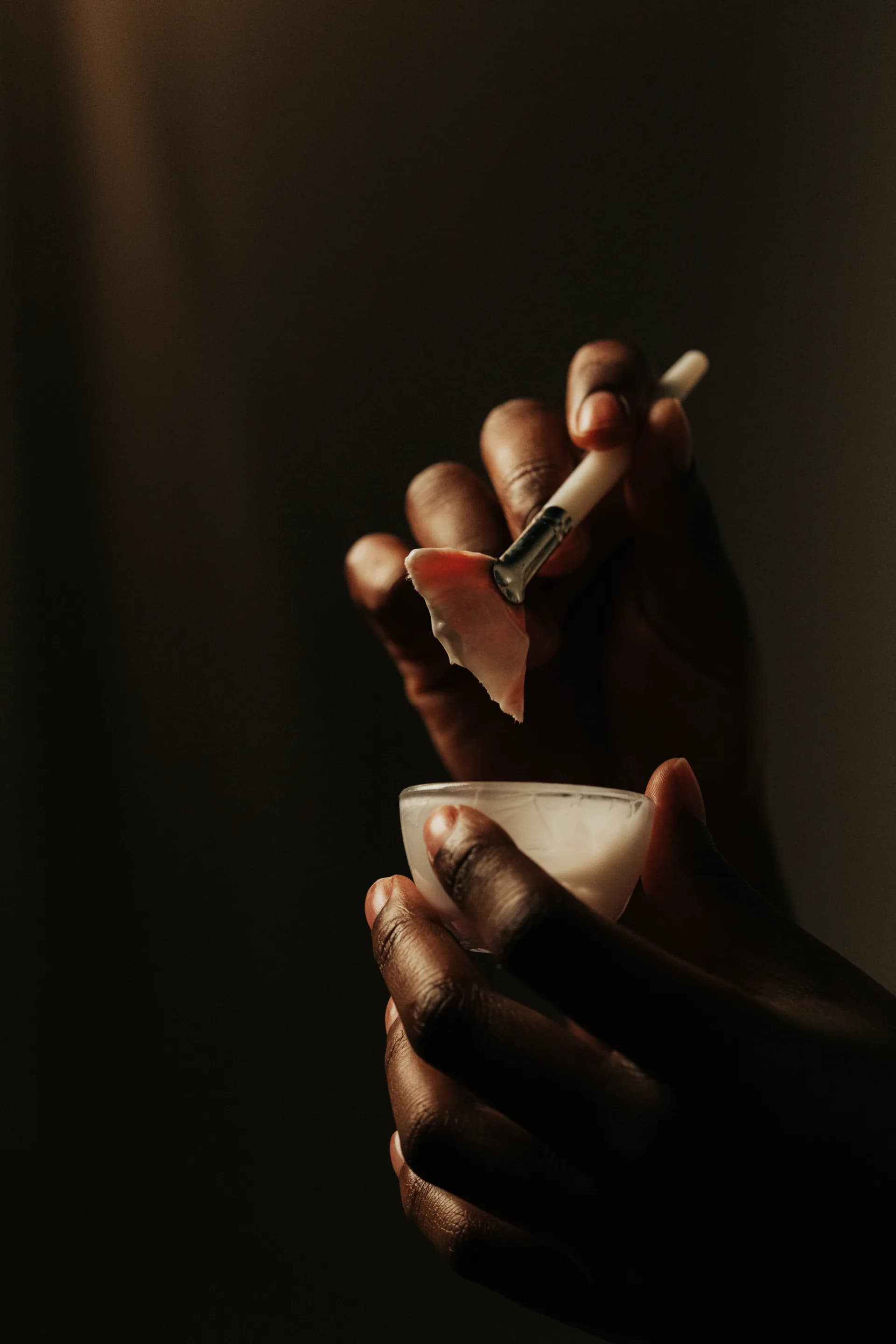 An esthetician's hands preparing a small dish of product with a brush