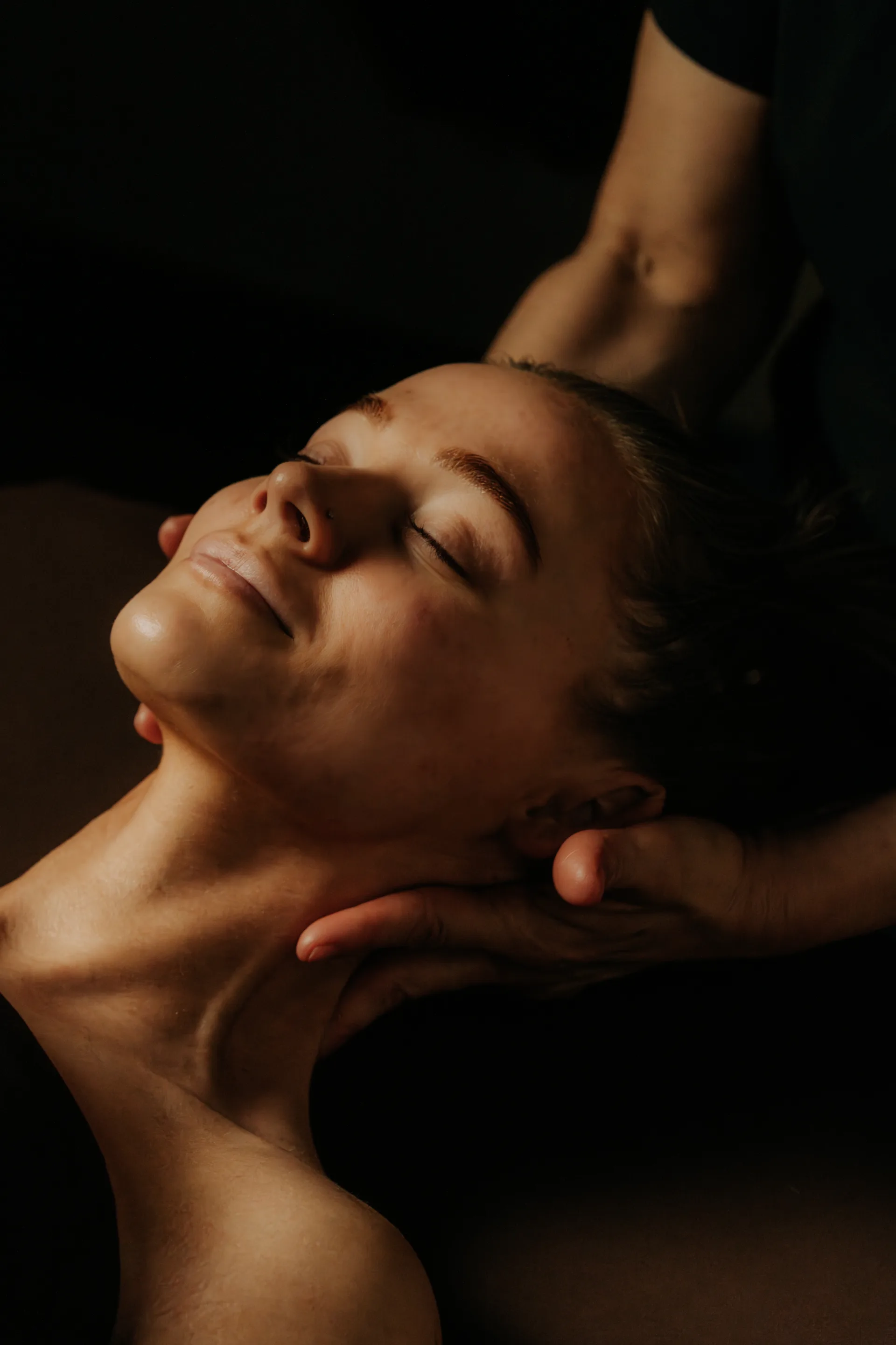 A massage therapist's hands easing a guest's neck and shoulders by candlelight